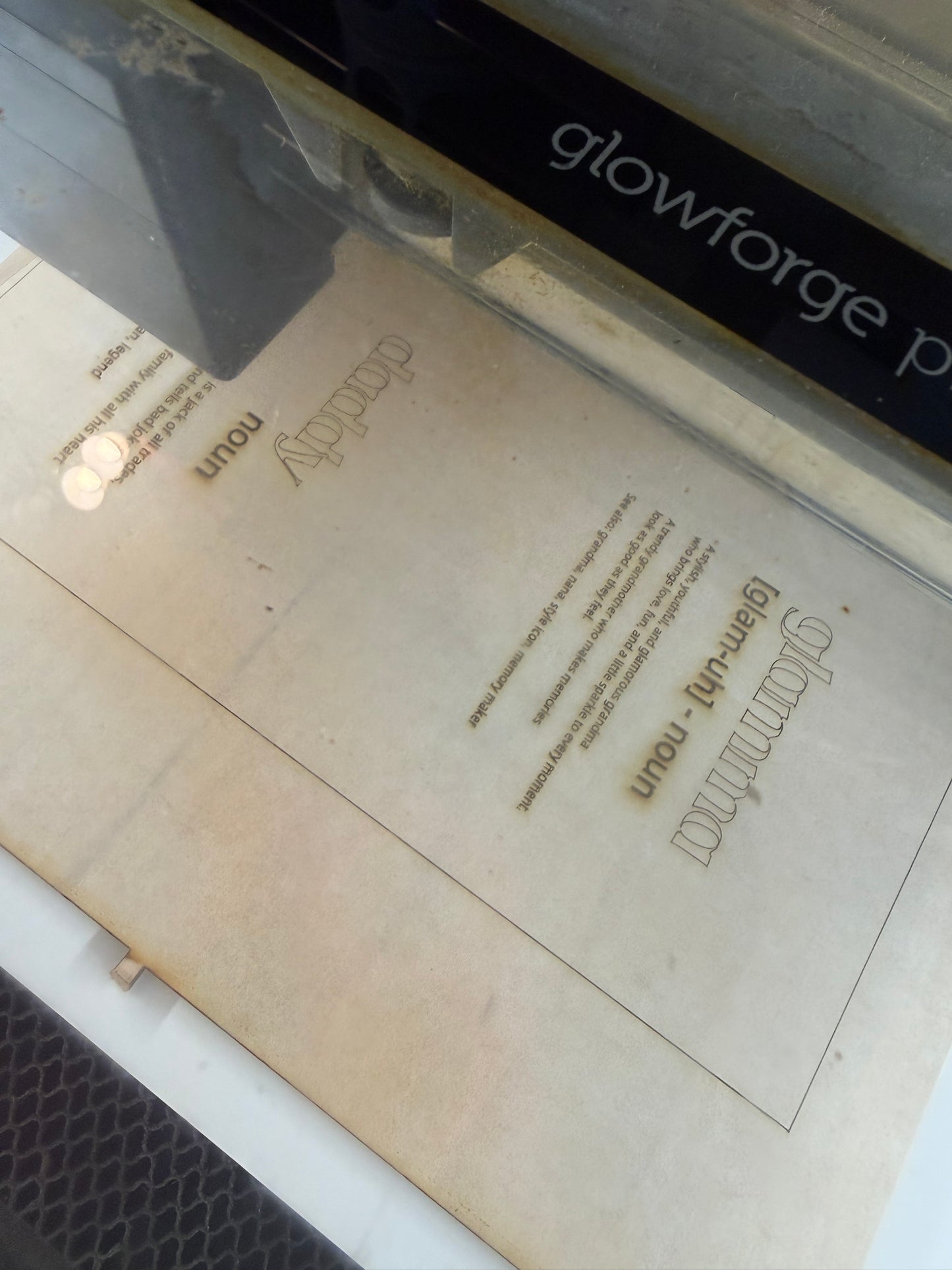 Glowforge laser in the process of engraving text on wood.