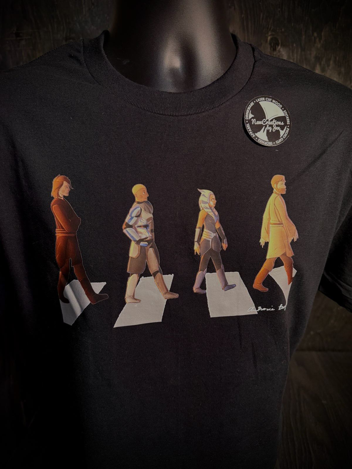 Black t-shirt with a graphic of four figures walking on a road, resembling the famous Abbey Road album cover, worn by a mannequin.